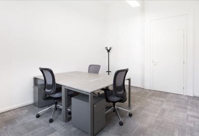 Minimalist private office with two light wood desks and black ergonomic chairs.