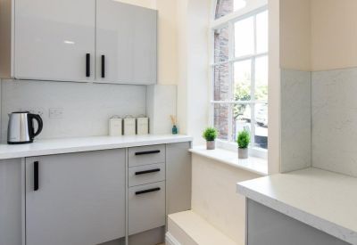 Modern communal kitchen with light grey cabinetry and a view through an arched window.