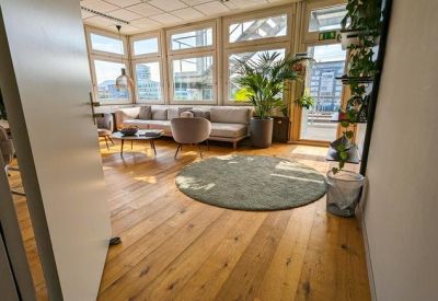 Bright breakout room with wooden floors, grey sofas, and large windows.