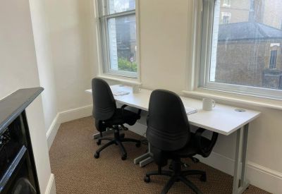 Two-person workspace with white desks and black chairs positioned near bright windows.
