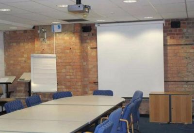 Professional meeting room featuring a large conference table, projector screen, and exposed brick walls.