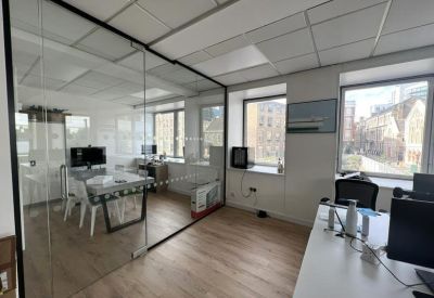 Private glass-partitioned meeting room adjacent to a bright open-plan workspace.