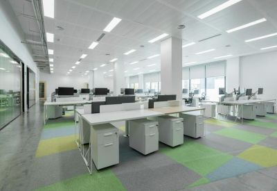 Spacious office interior with rows of white desks and green and blue carpet tiles.