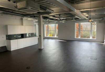 Open-plan office space featuring a kitchenette, exposed ceilings, and large windows.