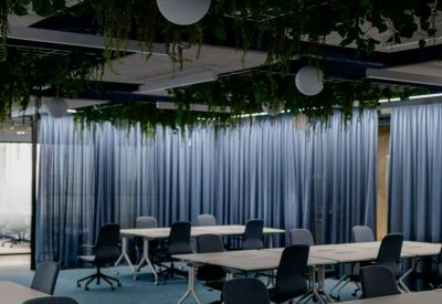 Open-plan office with multiple white desks, ergonomic chairs, and a ceiling installation of hanging plants.