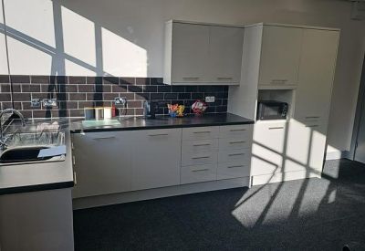 Modern communal kitchen with grey cabinetry, dark tiled backsplash, and natural light.