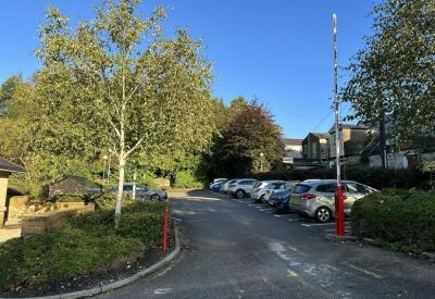 Surface parking lot with several cars parked alongside green trees and a security barrier.