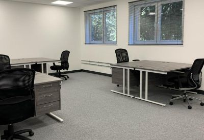 Bright, open-plan office space with grey desks and black mesh chairs.