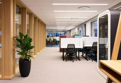 Bright hallway with glass-walled offices, indoor plants, and a private phone booth.