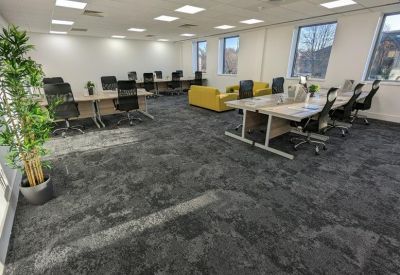 Spacious open-plan office with grey carpeting and rows of modern desks.