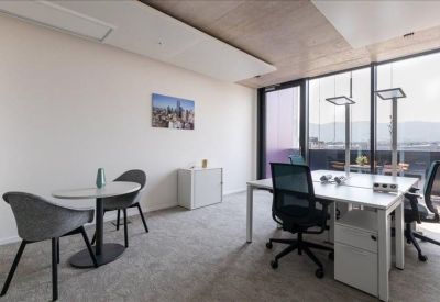 Bright corner office with two white desks and a small meeting table.