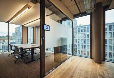 Private glass-walled office featuring two desks and a view of neighboring buildings.