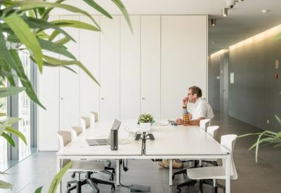 Bright coworking space with a long white table and floor-to-ceiling windows.