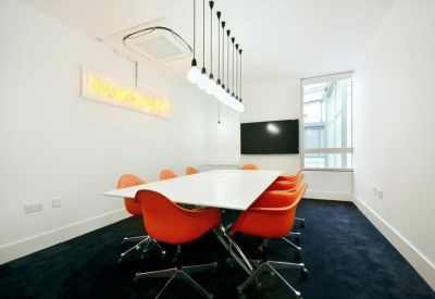 Modern meeting room with orange chairs, a long white table, and a neon sign.