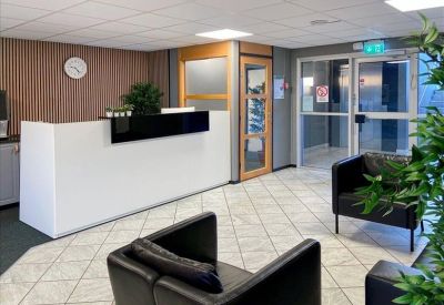 Bright reception area with a minimalist white desk, black armchairs, and wood-paneled walls.