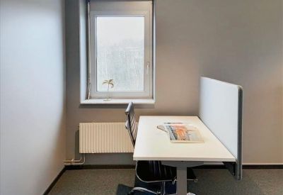 Private workstation by a window with a desk divider and black office chair.