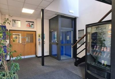 Reception area with a blue passenger lift, wooden double doors, and indoor greenery.