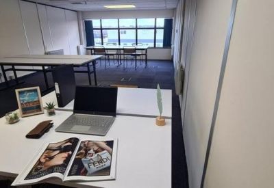 Modern workspace with a white desk, laptop, and a view into a secondary office area.