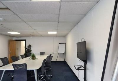 Spacious meeting room with a long white table, black mesh chairs, and a wall-mounted TV.