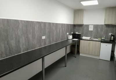 Long kitchen area with grey wall panels, a breakfast bar, and white appliances.