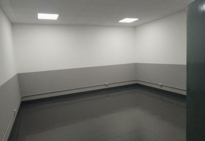 Empty office unit with grey flooring and white walls under bright square lights.