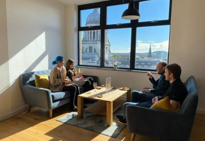 Bright lounge area with blue armchairs and a view of a domed building through the window.