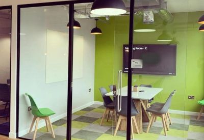 Glass-walled meeting room featuring a green accent wall and checkered carpet tiles.