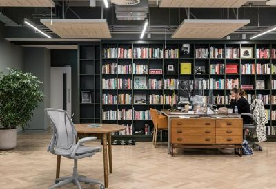 Open-plan office area with a long wooden library bookshelf and a large potted plant.