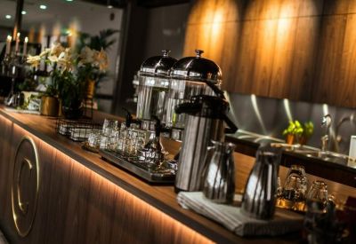 Communal cafe area with warm wood paneling, coffee machines, and glass carafes.