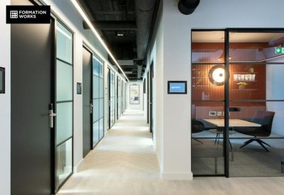 Bright office corridor featuring glass-walled suites and an integrated digital room booking screen.