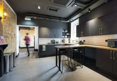 Modern communal kitchen and breakout area with black cabinetry and brick feature wall.