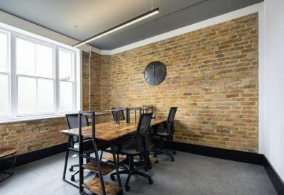 Four-person workstation with wooden desks against a classic brick wall.