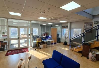 Bright reception lobby with a blue sofa, wooden floors, and a staircase.