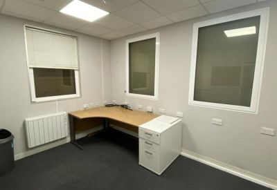 Private office suite featuring a corner desk, white filing cabinet, and multiple windows.