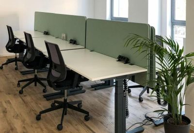 Open-plan workspace with multiple desks separated by sage green acoustic privacy screens.