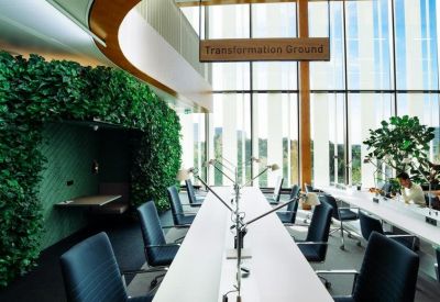 Spacious open-plan workspace featuring long white desks and a vibrant green living wall.
