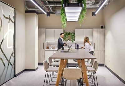 Communal breakout area featuring a long high table, modern stools, and hanging greenery.