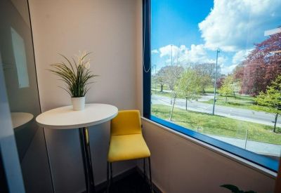 Small breakout nook with a yellow chair, white table, and large window overlooking trees.