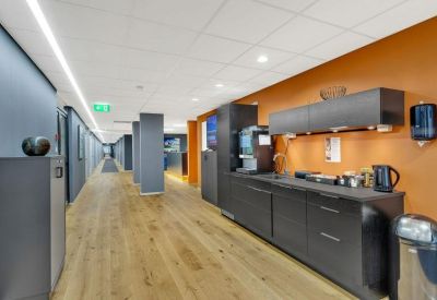 Modern communal kitchen and coffee station with dark cabinetry against a vibrant orange wall.