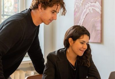 Two colleagues collaborating over a laptop in a bright office with a large window.
