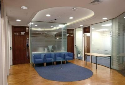Bright reception area featuring blue armchairs, glass partitions, and polished wooden floors.