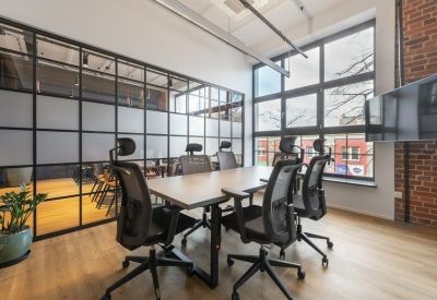 Bright conference room with a light wood table, mesh chairs, and large industrial windows.