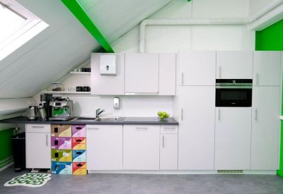 Modern white office kitchenette featuring built-in appliances and colorful storage crates.