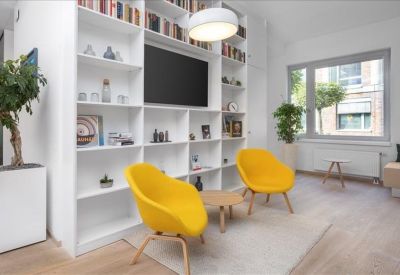 Modern lounge area with yellow tub chairs, a white bookshelf, and a flat-screen TV.