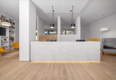 Modern reception lobby with a sleek white desk, pendant lighting, and warm wood flooring.