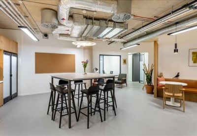 Modern breakout area with high stools, exposed ceiling pipes, and a cork notice board.