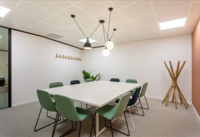 Bright meeting room with white table, green chairs, and modern pendant lighting.
