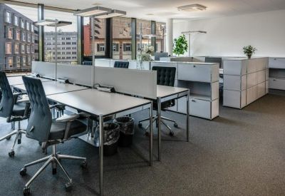 Open-plan office space with white desks and ergonomic black chairs.