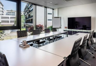 Spacious boardroom with a U-shaped table arrangement and video conferencing screen.
