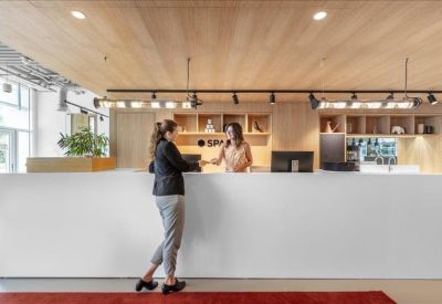 Close-up of a white minimalist reception desk with two staff members and light wood ceiling.